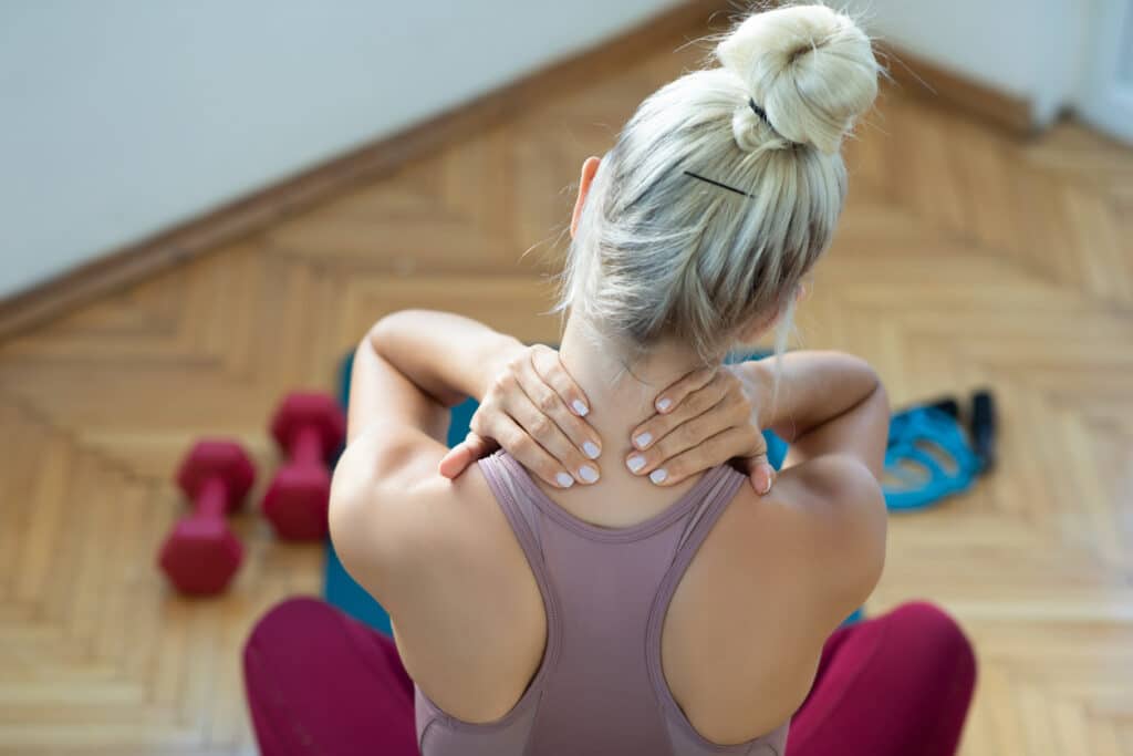 Woman holding the back of her neck after exercise, representing muscle tension and discomfort addressed with dry needling or cupping in physical therapy. Woman holding the back of her neck after exercise, representing muscle tension and discomfort addressed with dry needling or cupping in physical therapy.
